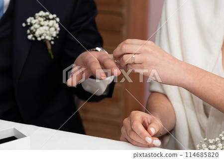 The bride puts a ring on the groom's finger 114685820