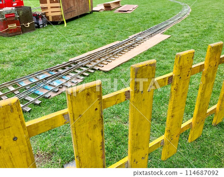 Mini train tracks and yellow fence on the grass 114687092