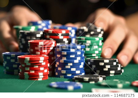 A poker player strategically adjusts stacks of colorful chips on a green felt table 114687175