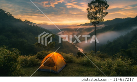 Tent on a hill overlooking a misty river valley at sunrise with a golden sky 114687217