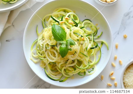 Zucchini noodles in a creamy sauce with basil and pine nuts, served in a bright white bowl 114687534