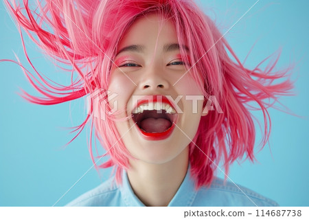 Radiant young woman with bright pink hair laughing heartily, against a light blue background 114687738