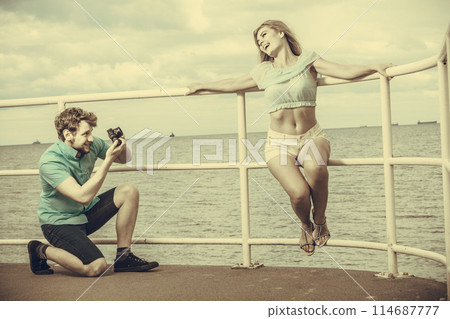 Young couple in love is taking photos on sea pier. Young couple in love is taking photos on sea pier. 114687777