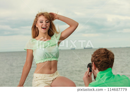 Young couple in love is taking photos on sea pier. Young couple in love is taking photos on sea pier. 114687779