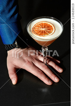 Male hand with glass of almond sour cocktail on black Male hand with glass of almond sour cocktail on black 114689019