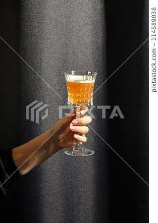 Female hand holding crystal glass of classic whiskey sour cocktail 114689038