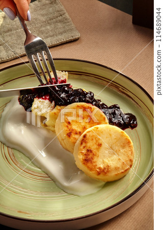 Female hands slicing syrniki served with berry topping and yoghurt cream 114689044