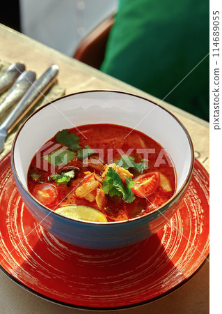 Spicy Thai tom yum soup in colorful bowl with dining setting 114689055