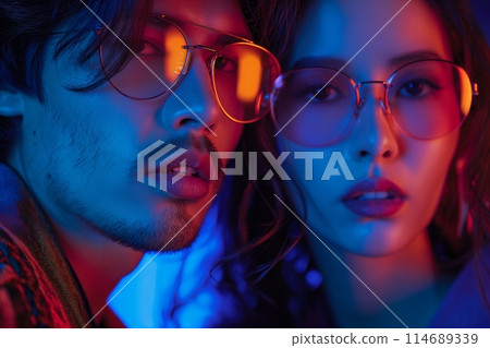 Intense portrait of a stylish couple in glasses, wrapped in a moody, neon lit atmosphere 114689339