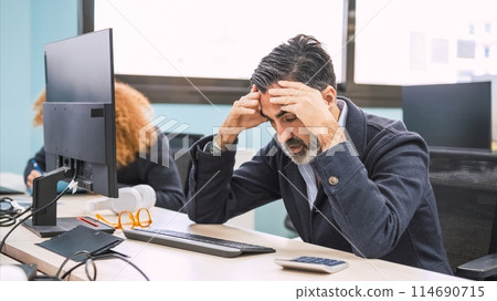 Stressed businessman sitting with head in hands at computer desk in office 114690715
