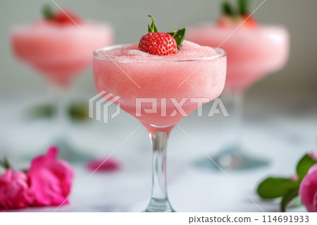Pink frothy cocktails frose garnished with mint and a flower, surrounded by vibrant pink blooms 114691933