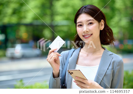 Young business woman holding a smartphone and a card Young business woman holding a smartphone and a card 114695357
