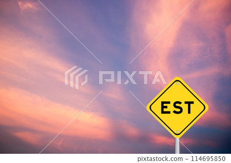 Yellow transportation sign with word EST  (abbreviation of established, estimated, eastern time zone, expressed sequence tag) on violet color sky background 114695850