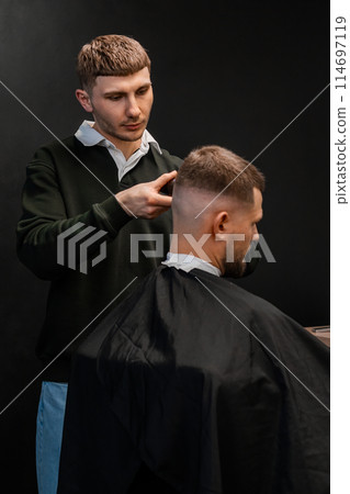 Skilled barber cuts client short hair with electrical trimmer in barbershop closeup. Hairdresser does stylish men haircut in beauty shop Skilled barber cuts client short hair with electrical trimmer in barbershop closeup. Hairdresser does stylish men haircut in beauty shop 114697119