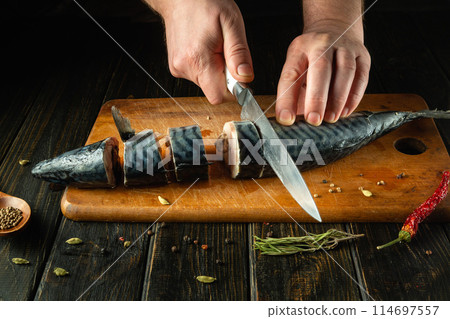The chef cuts mackerel fish into pieces to prepare a dish for dinner. Low key concept of fish diet. Advertising space 114697557