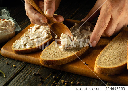Close-up of a chef hands using a spoon to add grated lard onto rye bread to prepare a delicious sandwich. Healthy fast food concept Close-up of a chef hands using a spoon to add grated lard onto rye bread to prepare a delicious sandwich. Healthy fast food concept 114697563