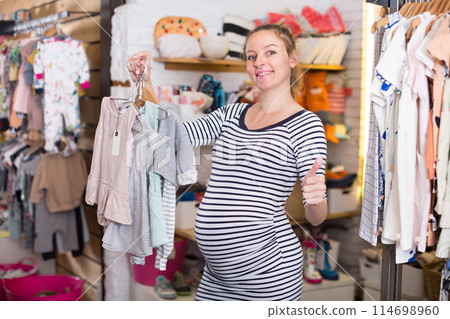 Pregnant woman In striped tunic chooses Dress for the future child 114698960