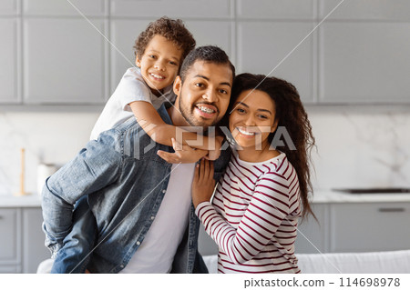 African American man and woman are standing in a kitchen, holding a child between them. Loving parents bonding with their cute son 114698978