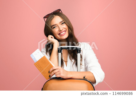 A woman is depicted holding a suitcase in one hand and a passport in the other. She appears ready to travel to another destination, perhaps for business or leisure purposes. 114699086