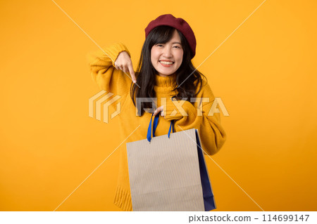 Young Asian woman in her 30s, wearing a yellow sweater and red beret, enjoys a shopping adventure against a vibrant yellow backdrop. 114699147
