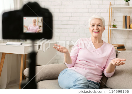 Experienced life coach. Friendly senior woman blogger sitting on sofa and recording video vlog at home 114699196