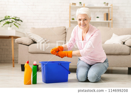 Domestic chores. Cheerful senior woman washing floor at home, smiling at camera with rag 114699208