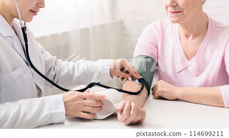 Female doctor measuring blood pressure of senior woman, healthcare concept 114699211