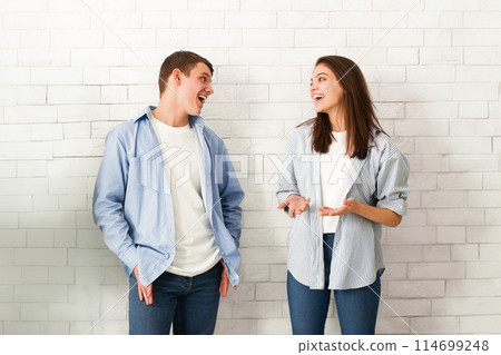 A guy and a girl are standing together in front of a brick wall, looking towards the camera with neutral expressions. Both are dressed casually. A guy and a girl are standing together in front of a brick wall, looking towards the camera with neutral expressions. Both are dressed casually. 114699248