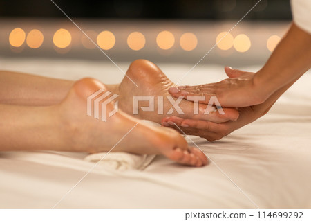 A person receives a soothing foot massage at a tranquil spa. The hands of a skilled masseur attend to the client, easing tension in their feet. A gentle, warm glow envelops the scene 114699292