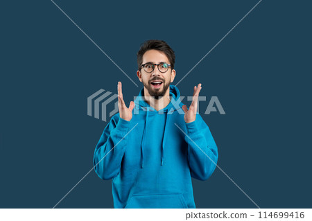 A man wearing a blue hoodie is seen gesturing with his hand in this photograph. The gesture appears to be deliberate and expressive, drawing attention to his actions. 114699416