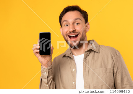 A man is holding up a cell phone in front of his face, focusing on the screen. He appears to be engaged with the device, showing nice app or online offer 114699420