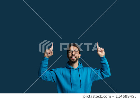 A man wearing a blue hoodie is standing with his hands raised in the air. He appears to be in a position of surrender or submission, copy space 114699453