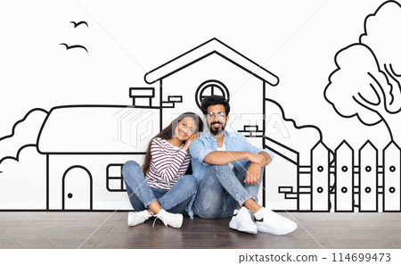 Cheerful young indian couple sitting by white wall with a house outline, dreaming of a home. Real estate, mortgage concept Cheerful young indian couple sitting by white wall with a house outline, dreaming of a home. Real estate, mortgage concept 114699473