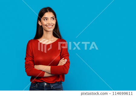 A woman wearing a red sweater stands with her arms crossed in a neutral pose. She appears confident and assertive with her body language, looking at copy space 114699611