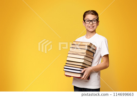 A young boy standing and holding a stack of books in his arms. 114699663