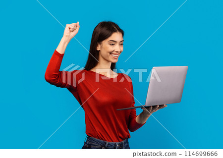 A woman wearing a red shirt is securely holding a laptop computer. Her fingers are visible on the keyboard, indicating she is using it, raising hand up, celebrating success A woman wearing a red shirt is securely holding a laptop computer. Her fingers are visible on the keyboard, indicating she is using it, raising hand up, celebrating success 114699666