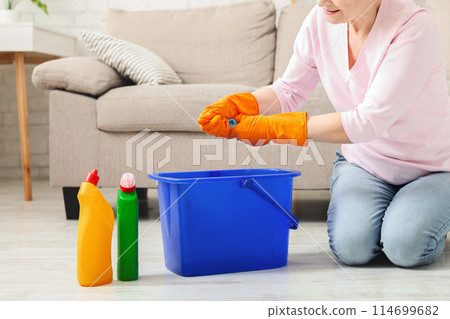Elderly woman kneeling, cleaning floor at home, empty space 114699682