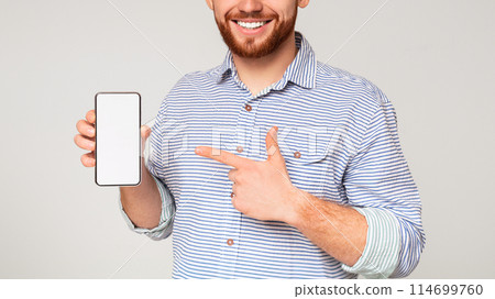 Smiling millennial man holding latest slim cellphone with blanc screen and pointing at it, panorama, free space Smiling millennial man holding latest slim cellphone with blanc screen and pointing at it, panorama, free space 114699760