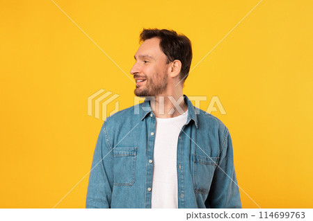 A man is depicted standing in front of a vivid yellow background. He is positioned centrally, facing aside, with both arms relaxed at his sides. 114699763