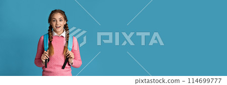 Surprised teenager girl with backpack posing on blue studio background, panorama with copy space. Education concept 114699777