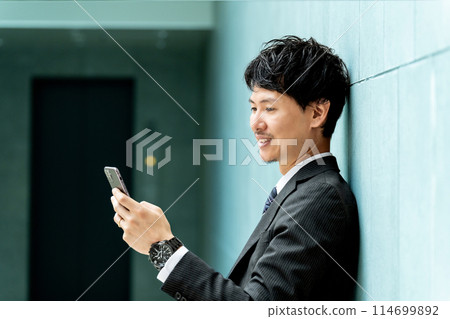 看智慧型手機螢幕的微笑的男性商人 看智慧型手機螢幕的微笑的男性商人 114699892