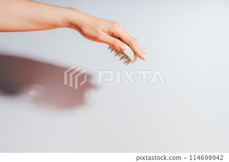 White massager for the scalp in the hand of the lady opposite the light background White massager for the scalp in the hand of the lady opposite the light background 114699942