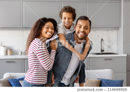 African American man, woman, and child are standing in the brightly lit living room. Happy black family posing together at home 114699989