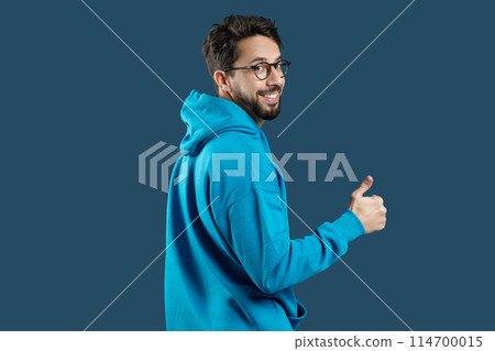 A man wearing a blue hoodie is shown in the image, raising his hand to give a thumbs up gesture. The mans face is not visible, and he appears to be standing against a plain background. 114700015