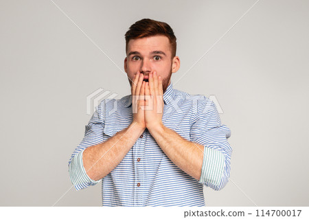Surprised guy. Shocked man holding his hends hiding open mouth on studio background, panorama, copy space Surprised guy. Shocked man holding his hends hiding open mouth on studio background, panorama, copy space 114700017