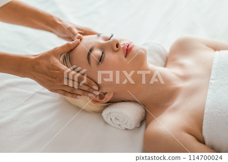 A serene spa setting where a young blonde woman receives a gentle facial massage, promoting a sense of relaxation and wellbeing 114700024