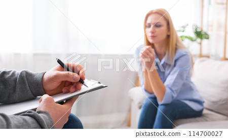 Psychotherapy. Therapist taking notes, listening to sad woman at personal consultation, empty space Psychotherapy. Therapist taking notes, listening to sad woman at personal consultation, empty space 114700027