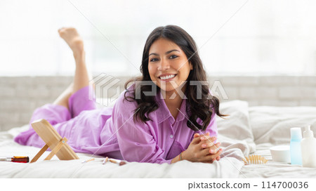 A middle eastern woman is reclining on a bed with her feet raised up in the air. She appears relaxed and comfortable in her position. A middle eastern woman is reclining on a bed with her feet raised up in the air. She appears relaxed and comfortable in her position. 114700036