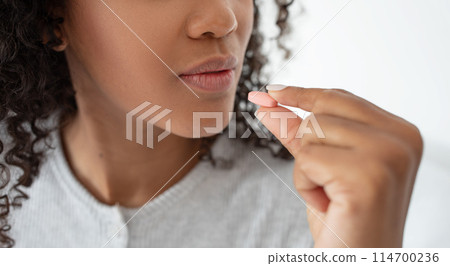 A close-up view captures a moment where a young woman with curly hair is about to consume a small pill, highlighting the importance of health and daily medication adherence, cropped A close-up view captures a moment where a young woman with curly hair is about to consume a small pill, highlighting the importance of health and daily medication adherence, cropped 114700236