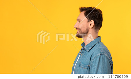 A man is standing in front of a bright yellow background. He is facing forward with a neutral expression. The background color contrasts sharply with his dark-colored clothing, copy space 114700309
